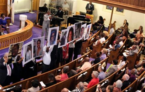 In this photo taken June 19, 2015, photos of the victims of the shooting at Emanuel AME Church in Charleston, S.C., are held during a vigil at the Metropolitan African Methodist Episcopal Church in Washington. The black church has long been the cornerstone and sanctuary for African American life. It has also long been a target for racists and white supremacists trying to strike blows against the African American psyche. The latest attack came Wednesday in Charleston, South Carolina, when 21-year-old Dylann Storm Roof joined a prayer meeting inside historic Emanuel African Methodist Episcopal Church and shot nine people dead, including the pastor, the Rev. Clementa Pinckney, and other ministers. (AP Photo/Glynn A. Hill)